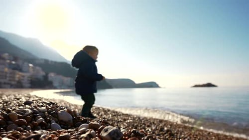 Toddler on Stony Coast Sea and Mountains in the Background