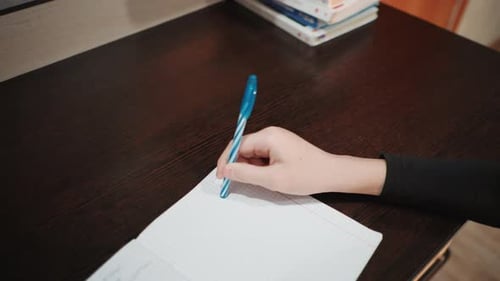 Child Writing Homework with Pen on Wooden Desk