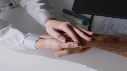 Hands of Female Doctor Consoling Distressed Male Patient in Clinic