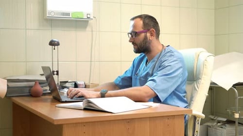 Young, Male Doctor Working on Laptop Sitting by Table in Office 30s