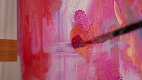 Close-up of a girl artist with a brush applying oil paint to a painting standing on an easel