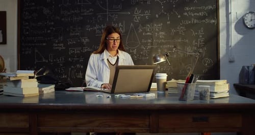 Female Scientist on Laptop in Front of Chalkboard