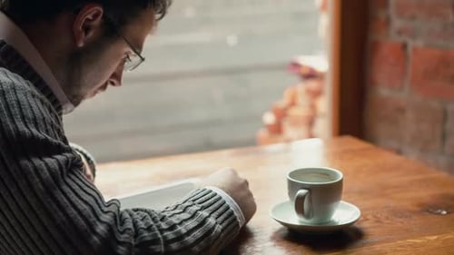Young Man Drinking Coffee in Cafe and Using Tablet Computer