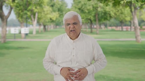 Sick Indian old man suffering from stomach pain in park