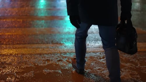 Nighttime Urban Crosswalk Scene with a Pedestrian in a Dark Coat and Gloves Carrying a Bag Walking