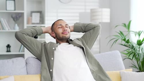 Man Relaxes on Sofa With Hands Behind Head
