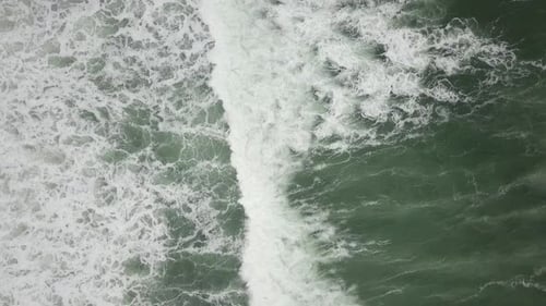 Stormy sea with waves breaking, white foam and beach sand dragged into the sea