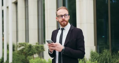 Successful young businessman stading near building office after workday using mobile phone