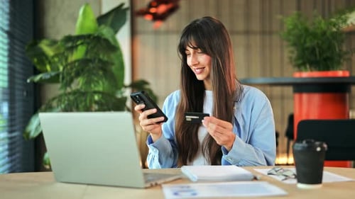 Mulher feliz fazendo pagamento on-line com cartão de crédito e smartphone no escritório