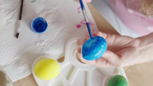 Woman painting Easter egg at home with pastel paints
