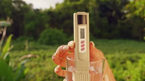 Close View Of Female Hand Holding Glass With Digital Water Quality Tester Showing Twenty Ppm Ppm