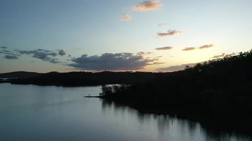Ascending drone shot flying over Wivenhoe Dam Lake, Camera Facing Sun at sunset. Landscape silhouett