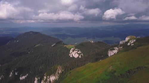 An aerial drone shot moving backward revealing a green mountain landscape.