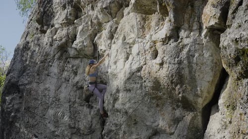 A Female Rock Climber Climbs a Route on a Rock in a Protective Helmet with a Rope