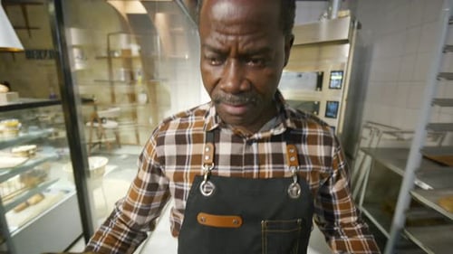 Senior Bakery Worker Walking with Tray of Fresh Croissants in Kitchen