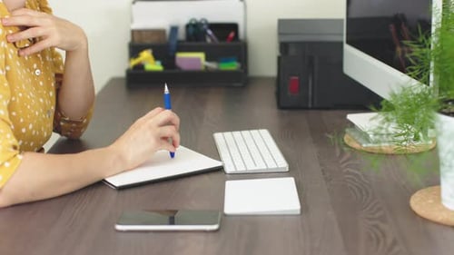 Adult writes in notebook at home office desk