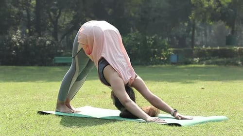 Video of Indian woman doing Adho Mukha svanasana in park.