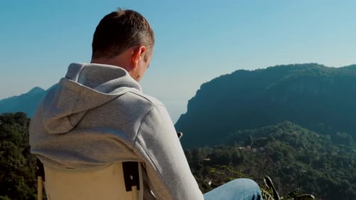 Man Sits Contemplatively Overlooking Green Mountain Range