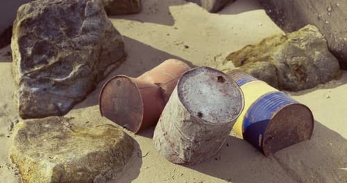 Rusty Cans and Rocks on Sandy Beach During Daylight