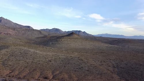Aerial shot of a single, lone hill peaking through the desert landscape with stunning mountains in t