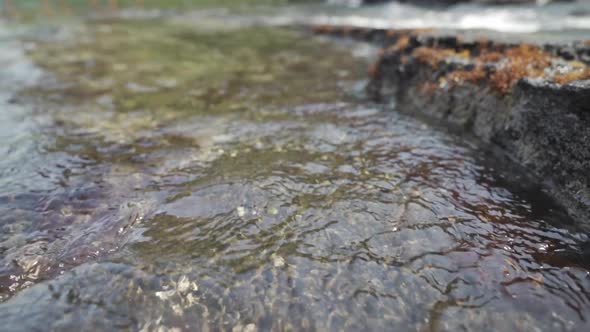 Sea water rushing in and rippling over lava rock with seaweed near ...