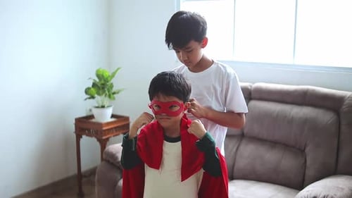 Boy Helping Younger Brother with Superhero Costume Indoors
