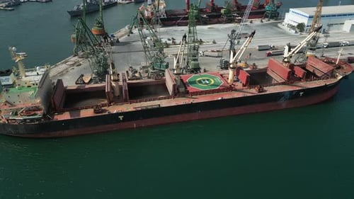 Aerial View of a Bustling Seaport Where a Massive Cargo Ship a Bulk Carrier is Being Loaded with