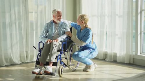 Blonde Nurse Talking to Senior Man in Wheelchair