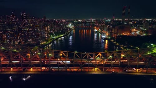 Multiple cars crossing the bridge at night. City lights reflecting in the river water.