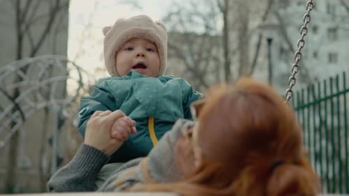 Fröhliche Mutter spielt mit ihrem Baby auf einer Schaukel auf einem Spielplatz