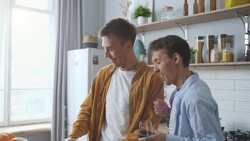 Two Young Men Cooking and Drinking Wine at Home