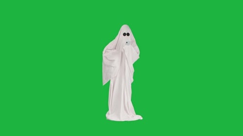 Halloween Ghost in White Sheet Watching Funny Video on Smartphone and Laughing Isolated on Chroma