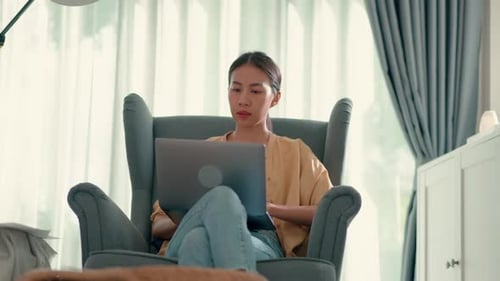 Young Adult Woman Uses Laptop in Cozy Armchair
