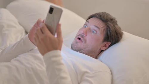 Mature Adult Man Shocked by Loss on Phone while Lying in Bed