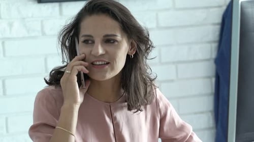 Young Businesswoman Talking on Cellphone Sitting by Desk in Office Adult