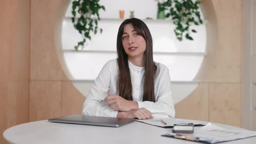 Woman Speaking at Table with Laptop and Papers