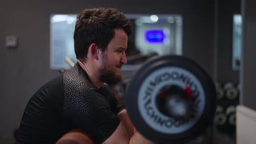 Bearded determined male perform seated barbell biceps curl at indoor gym