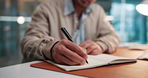 Man Writes in Notebook at Desk in Office