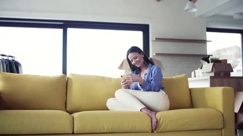 Woman using phone on a yellow couch indoors