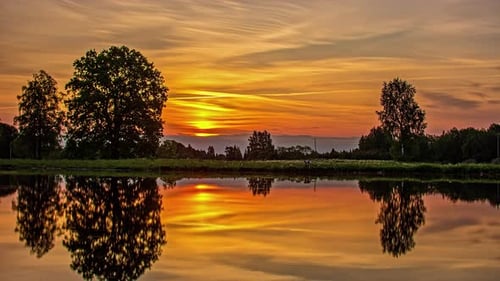 Vibrant sunrise with the golden sky reflecting off the surface of a lake - time lapse
