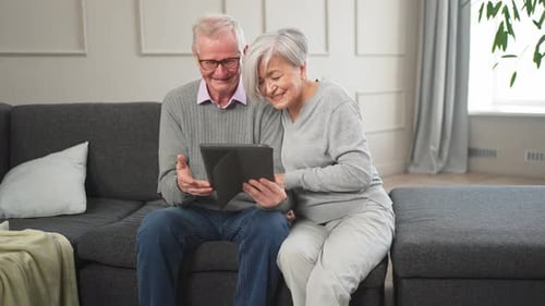 Senior Couple Enjoying Tablet Together on Gray Sofa