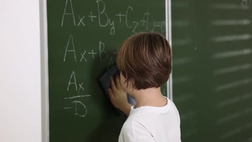 Boy Erases Math Equations on Chalkboard in Classroom