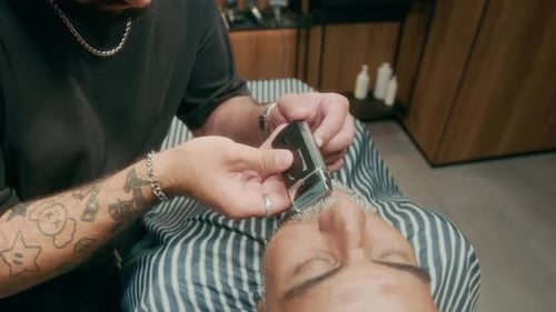 Tätowierter Barbier stylt Schnurrbart und Bart für ältere Kunden mit Rasierapparat