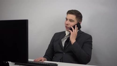 A Businessman Sits in an Office and Speaks on the Phone