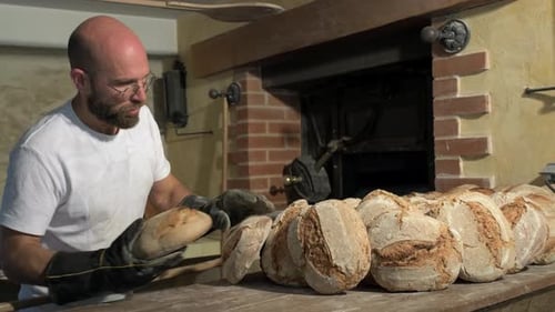 großer Seitenschuss, Bäckerhand mit Handschuhen nimmt das Brot aus der Schale und legt es neben