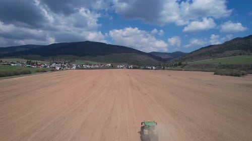Aerial following shot of a farmer cutting his field with a tractor in time for the new season