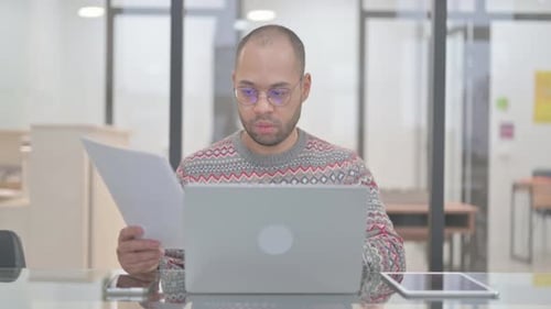 Man Reviews Documents While Working on Laptop