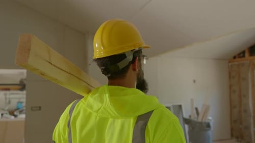 A Construction Worker is Seen Carrying Lumber in a Newly Renovated Interior Space Area