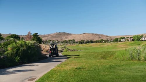 Wide shot of a winding golf path with a cart in motion, surrounded by dry hillside terrain and