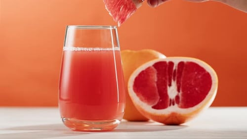 Hand Places Grapefruit on Glass of Juice